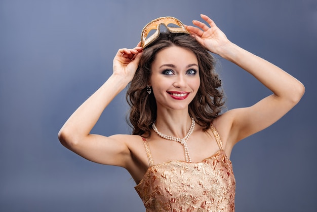 Donna felice in un abito d&#39;oro e collana di perle che indossa una maschera di carnevale sopra la sua testa