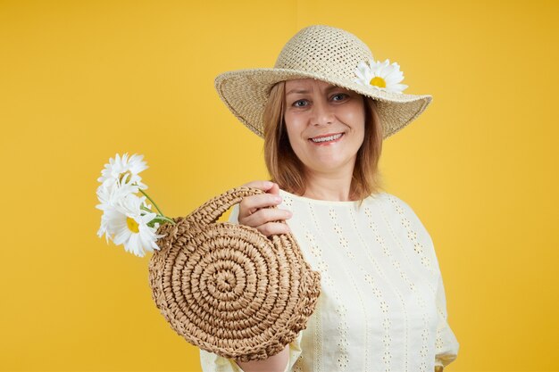 Donna felice in un cappello di paglia con una borsa di paglia su uno sfondo giallo brillante. Concetto di vendita estiva, vacanze estive.