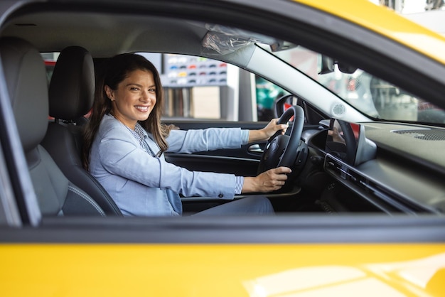 Donna felice in una macchina nuova ragazza bella che guarda dal finestrino della macchina donna d'affari che sceglie una macchina nuova in una concessionaria di auto
