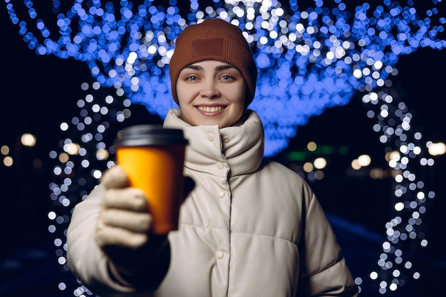 donna felice in vestiti caldi che mostra tazza gialla vuota di caffè da asporto e sorridente