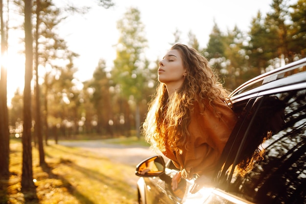 Donna felice in viaggio d'estate viaggia appoggiandosi fuori dal finestrino dell'auto Stile di vita attivo Concetto di viaggio