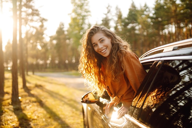 Donna felice in viaggio d'estate viaggia appoggiandosi fuori dal finestrino dell'auto Stile di vita attivo Concetto di viaggio