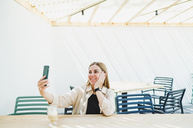 Donna felice seduta al tavolo di un caffè all'aperto e che parla al telefono con una tazza di caffè. Donna sorridente che si diverte a lavorare da casa in un caffè o a studiare online.