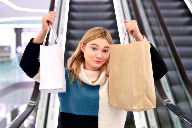 Donna felice shopping nel centro commerciale con sacchetti di carta, sorridente guardando la fotocamera