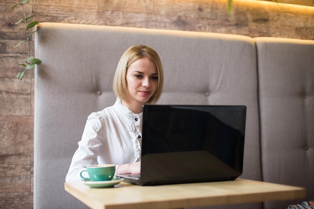 Donna felice utilizzando il computer portatile al caffè Giovane bella ragazza seduta in un bar e lavorando sul computer