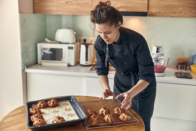 Donna fiduciosa professionale sta preparando torte di crema pasticcera in cucina moderna leggera a casa