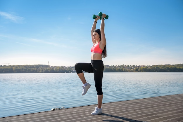 Donna fitness che fa esercizio mattutino con piccoli pesi del lago of