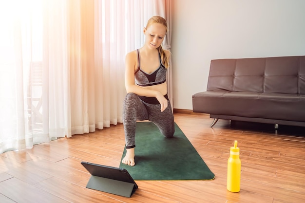 Donna fitness che si esercita sul pavimento a casa e guarda video di fitness in un tablet Le persone fanno sport online a causa del coronovirus