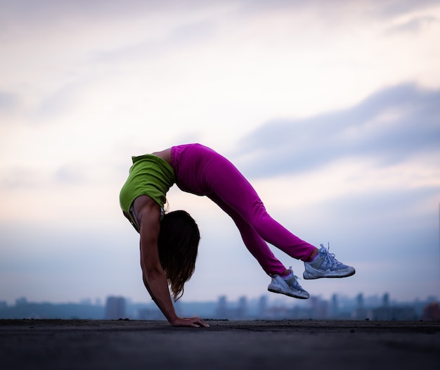 Donna flessibile che fa verticale all'aperto sullo sfondo del tramonto drammatico concetto di yoga e salute