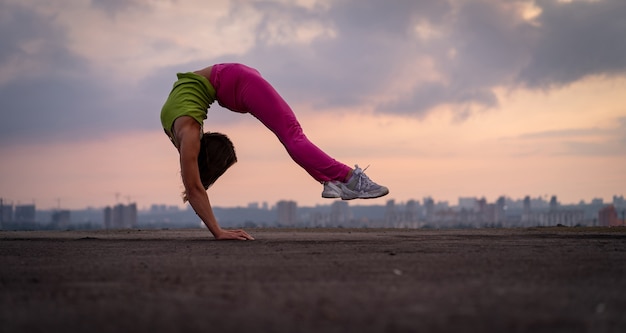 Donna flessibile che fa verticale all'aperto sullo sfondo del tramonto drammatico concetto di yoga e salute