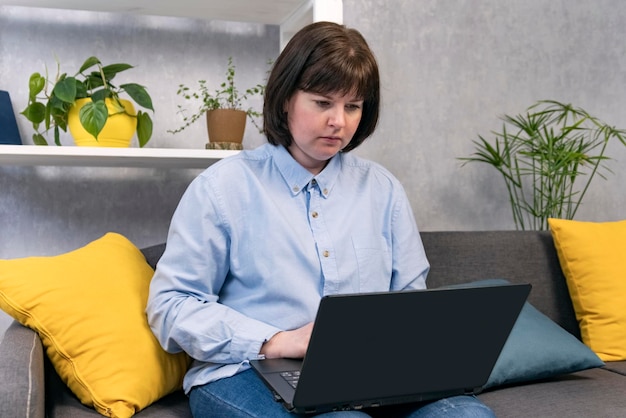 Donna focalizzata che lavora al computer portatile sul divano di casa. Donna d'affari, libera professionista.