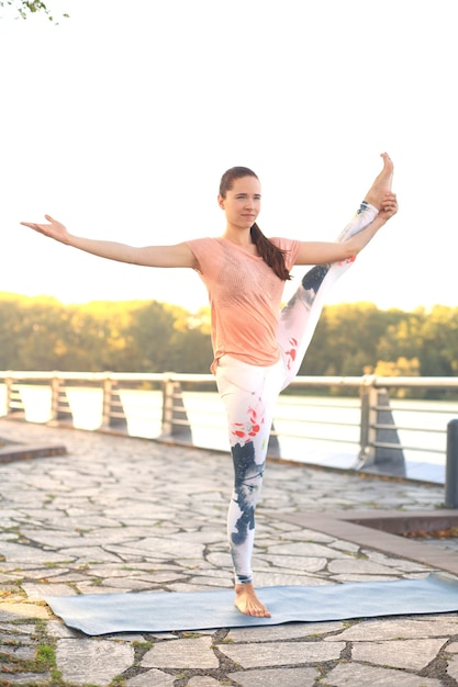 Donna forte atletica che pratica posa difficile di yoga all'aperto.