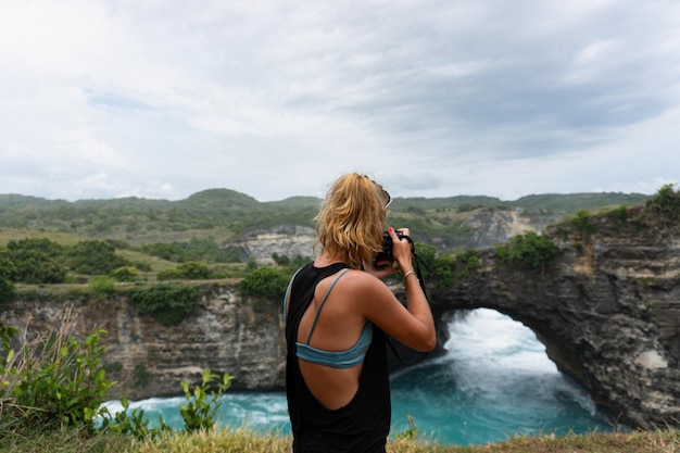 Donna fotografo viaggiatore che fotografa i punti di riferimento sulla fotocamera, la spiaggia di Angel's Billabong, l'isola di Nusa Penida, Bali, Indonesia.