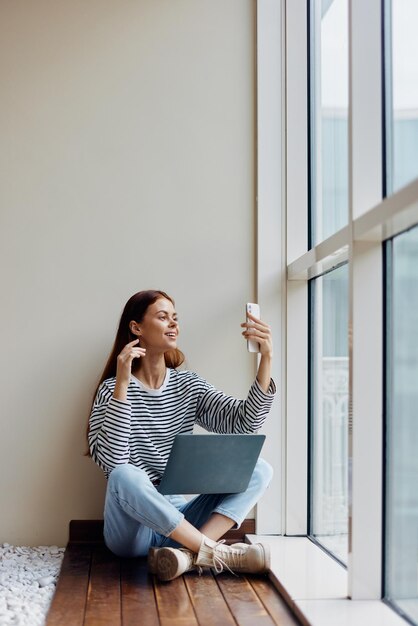 Donna freelance seduta con laptop e telefono alla finestra videochiamata felicità del lavoro online