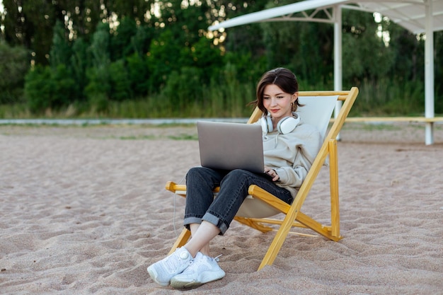Donna freelance seduta su un lettino e che lavora al computer sulla riva del lago