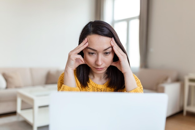 Donna frustrata che lavora dall'ufficio a casa davanti al laptop che soffre di mal di testa cronico quotidiano trattamento online nominando a una consulenza medica radiazioni elettromagnetiche paga per malattia