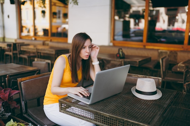 Donna frustrata nella caffetteria all'aperto di strada seduta al tavolo lavorando su un moderno computer portatile, ristorante durante il tempo libero free