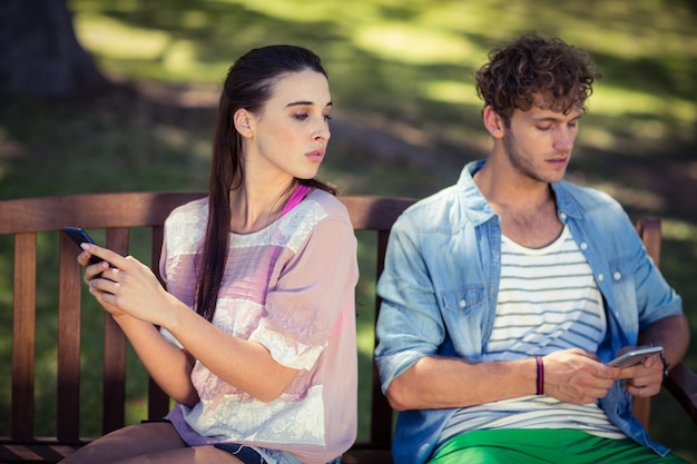 Donna gelosa che spia il telefono cellulare del suo uomo in parco