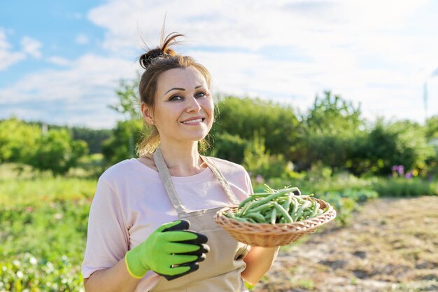 Donna giardiniere agricoltore con cesto di fagiolini verdi freschi raccolto naturale sano cibo biologico estate orto sfondo