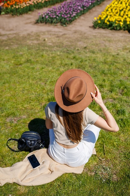 Donna gioiosa con cappello di paglia seduto tra il campo di tulipani in serra