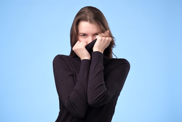 Donna gioiosa in maglione blu alla moda che nasconde la faccia essendo di umore giocoso