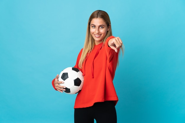 Donna giovane calciatore isolata sulla parete blu che punta davanti con felice espressione