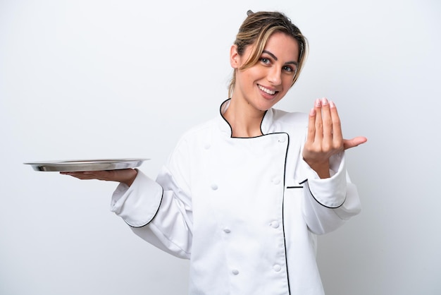 Donna giovane chef con vassoio isolato su sfondo bianco che invita a venire con la mano Felice che tu sia venuto