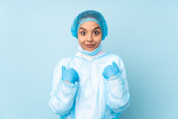 Donna giovane chirurgo in uniforme blu con espressione facciale a sorpresa