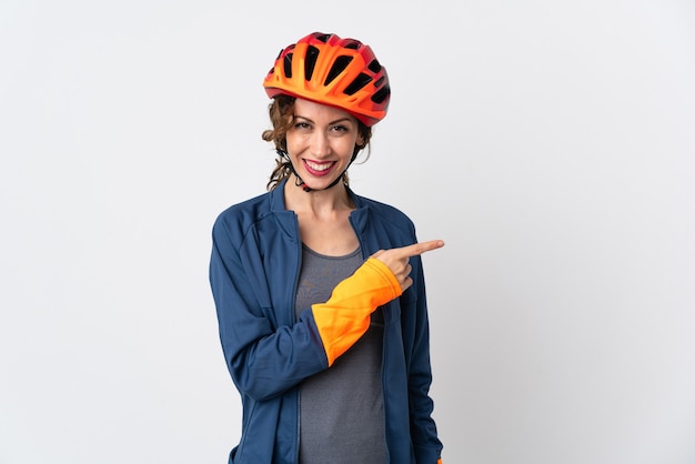 Donna giovane ciclista isolata sul muro bianco che punta il dito a lato