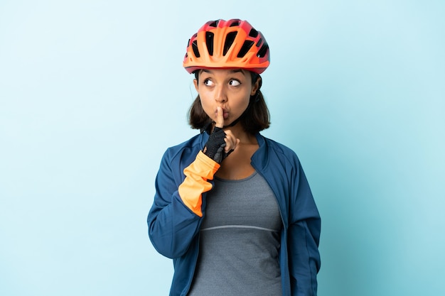 Donna giovane ciclista isolata sull'azzurro che mostra un segno di gesto di silenzio che mette il dito in bocca