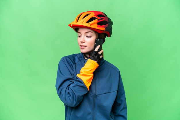 Donna giovane ciclista su sfondo chroma key isolato mantenendo una conversazione con il telefono cellulare con qualcuno