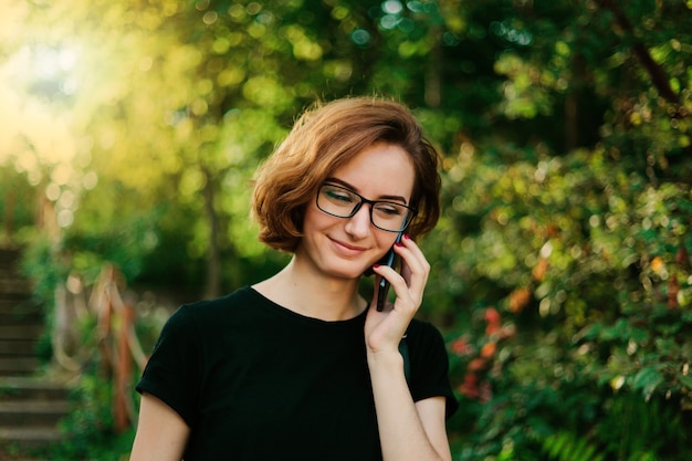 Donna giovane hipster in bicchieri parlando al telefono all'aperto