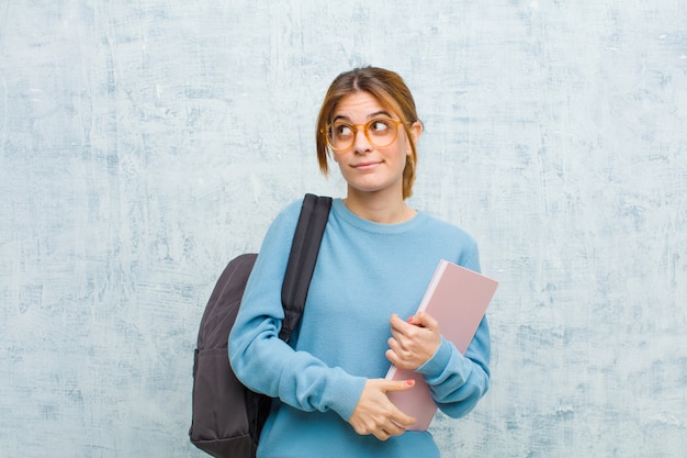 Donna giovane studente chiedendo, pensando pensieri e idee felici, sognare ad occhi aperti, cercando di copiare lo spazio sul lato sulla parete del grunge