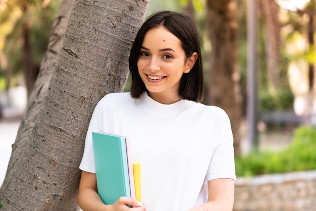 Donna giovane studente felice che tiene i taccuini all'aperto