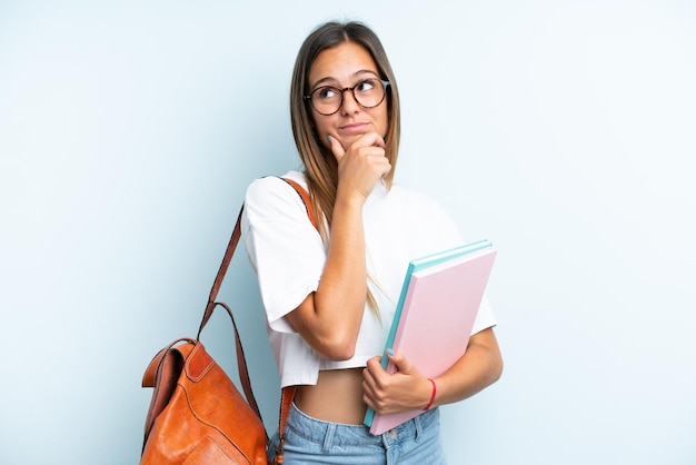 Donna giovane studente isolata su sfondo blu avendo dubbi