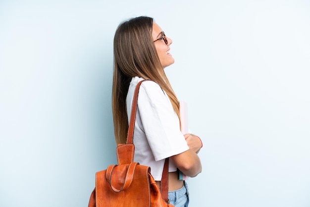 Donna giovane studente isolata su sfondo blu che ride in posizione laterale