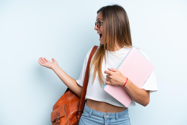 Donna giovane studente isolata su sfondo blu con espressione di sorpresa mentre guarda di lato