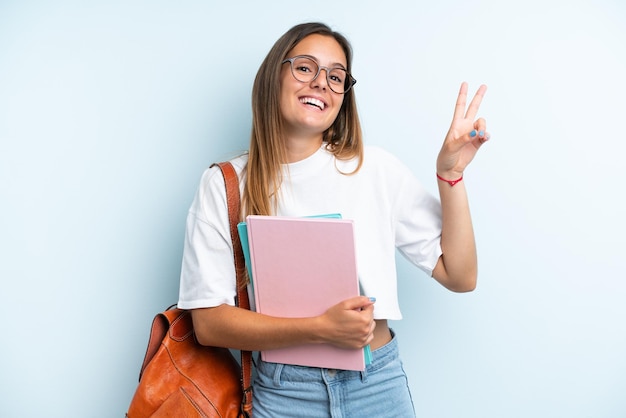 Donna giovane studente isolata su sfondo blu sorridendo e mostrando il segno di vittoria