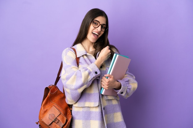 Donna giovane studente isolata su sfondo viola che celebra una vittoria