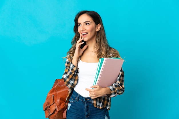 Donna giovane studente isolata sulla parete blu che pensa un'idea mentre osserva in su