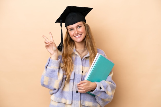 Donna giovane studente su sfondo isolato sorridendo e mostrando il segno di vittoria