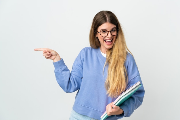 Donna giovane studentessa bionda isolata su sfondo bianco sorpreso e puntare il dito a lato