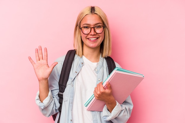 Donna giovane studentessa venezuelana isolata sul muro rosa sorridente allegro che mostra il numero cinque con le dita.