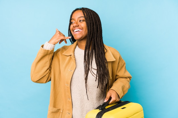Donna giovane viaggiatore afroamericano che tiene una valigia isolata che mostra un gesto di chiamata di telefono cellulare con le dita.
