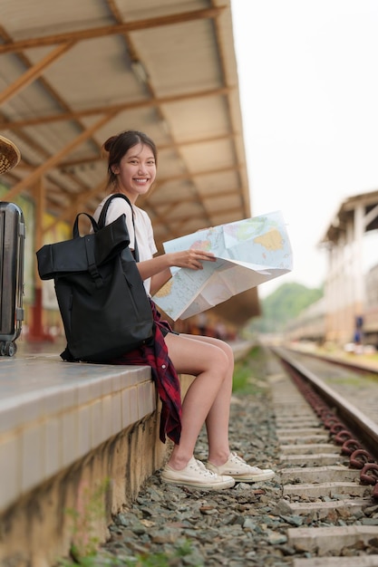 Donna giovane viaggiatore che guarda le mappe che pianificano il viaggio alla stazione ferroviaria Concetto di stile di vita estivo e di viaggio