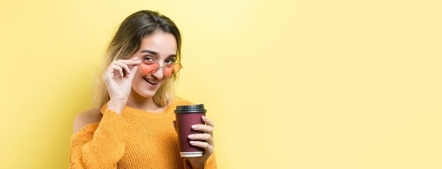 Donna glamour con gli occhiali in un maglione arancione con una bevanda di caffè su sfondo giallo