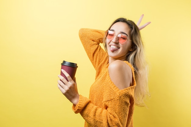 Donna glamour con gli occhiali in un maglione arancione con una bevanda di caffè su sfondo giallo