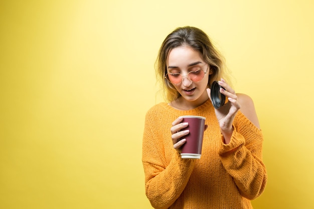 Donna glamour con gli occhiali in un maglione arancione con una bevanda di caffè su sfondo giallo