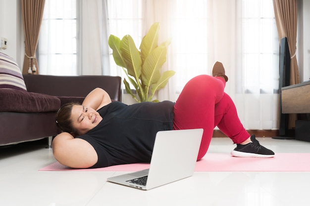 Donna grassa asiatica che si esercita e sta usando un computer portatile a casa, concetto di idea sportiva e ricreativa.