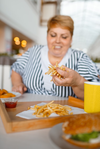 Donna grassa che mangia cibo ad alto contenuto calorico nel centro commerciale